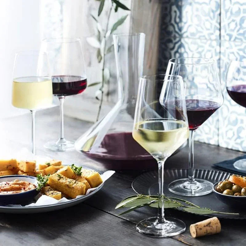 Elegant wine glasses with red and white wine, decanter, and appetizers on dark table for dining setup