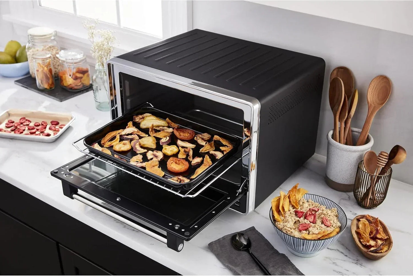 Black countertop oven baking dried fruit slices on a tray in a modern kitchen setting