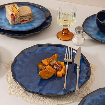 Blue ceramic dinner plates with scalloped edges, serving sandwiches and roasted squash, paired with silverware and lace placemats.