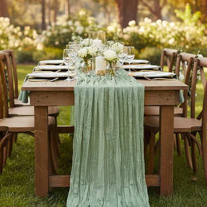 Mint green pleated table runner on rustic outdoor dining table with white roses, candles, and glassware