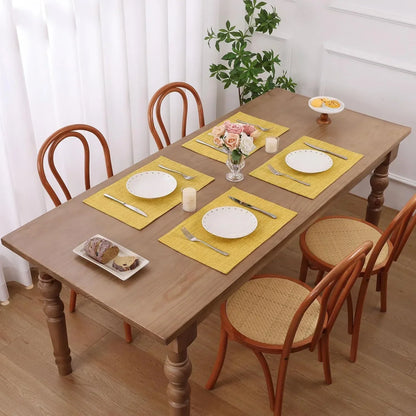 Yellow woven placemats on wooden dining table with white plates, cutlery, and floral centerpiece for elegant table setting