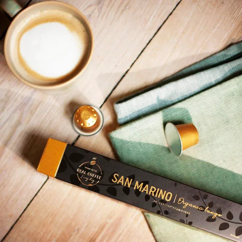 San Marino Organic Lungo coffee capsules with frothy latte on wooden table, kitchen routine essentials