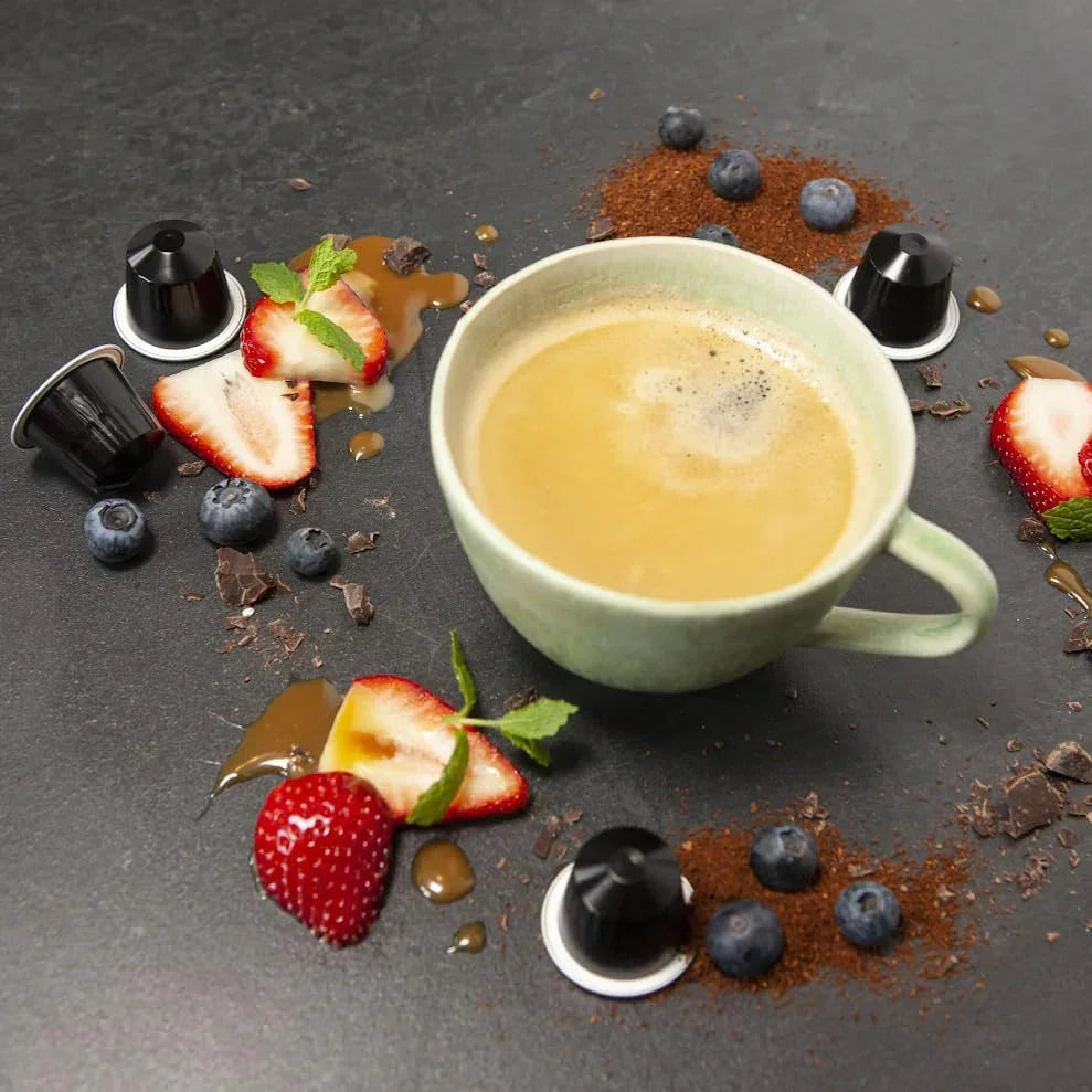 Fresh coffee in ceramic mug with strawberries, blueberries, chocolate, and coffee pods on dark surface