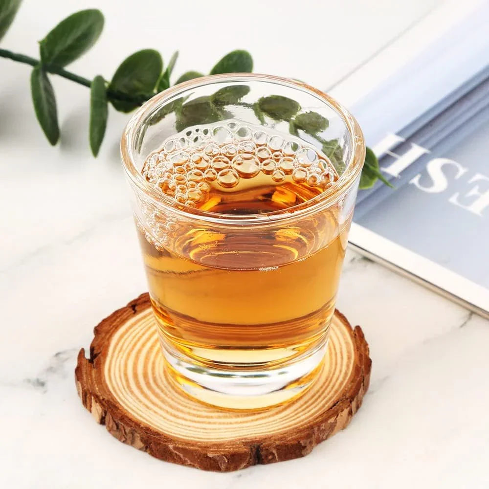 Clear glass tumbler with amber liquid on rustic wood coaster, green leaf accent, ideal for kitchen drinkware