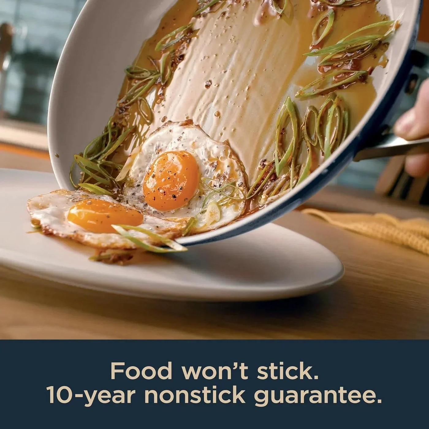 Nonstick frying pan with sunny-side-up eggs and greens sliding onto plate, 10-year guarantee