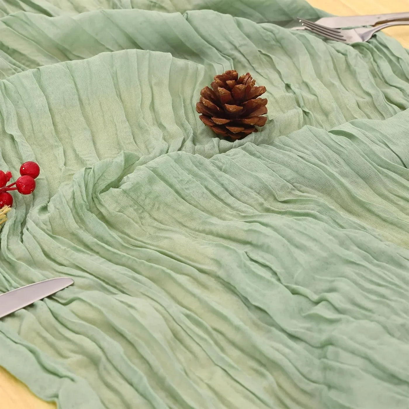 Mint green crinkled table runner with pinecone, red berries, and silverware for festive kitchen decor