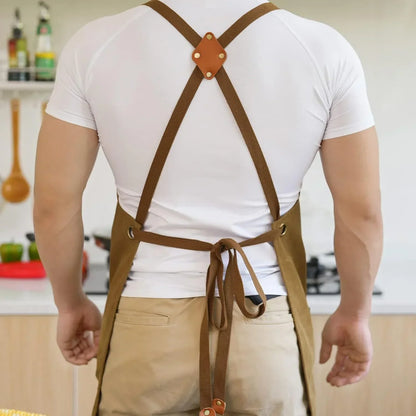 Brown canvas apron with cross-back straps and leather accents, worn in a kitchen setting