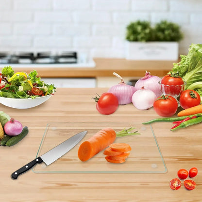 Glass cutting board with chef knife slicing carrot on wooden kitchen counter surrounded by fresh veggies
