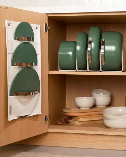 Green cookware set organized in wooden cabinet with hanging lid organizer and white bowls