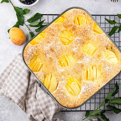 Freshly baked apple cake with powdered sugar, served on a cooling rack with apricot and green leaves.