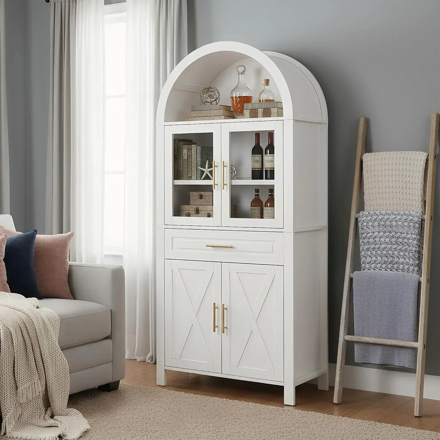 White arched storage cabinet with glass doors, gold handles, and wine bottles displayed in a cozy living room