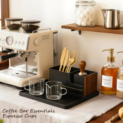 Cream espresso machine with glass cups, gold cutlery, and coffee syrups on a kitchen counter