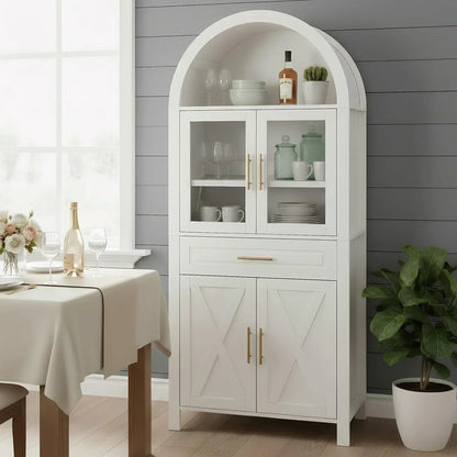 White arched kitchen storage cabinet with glass doors, gold handles, and dining table nearby