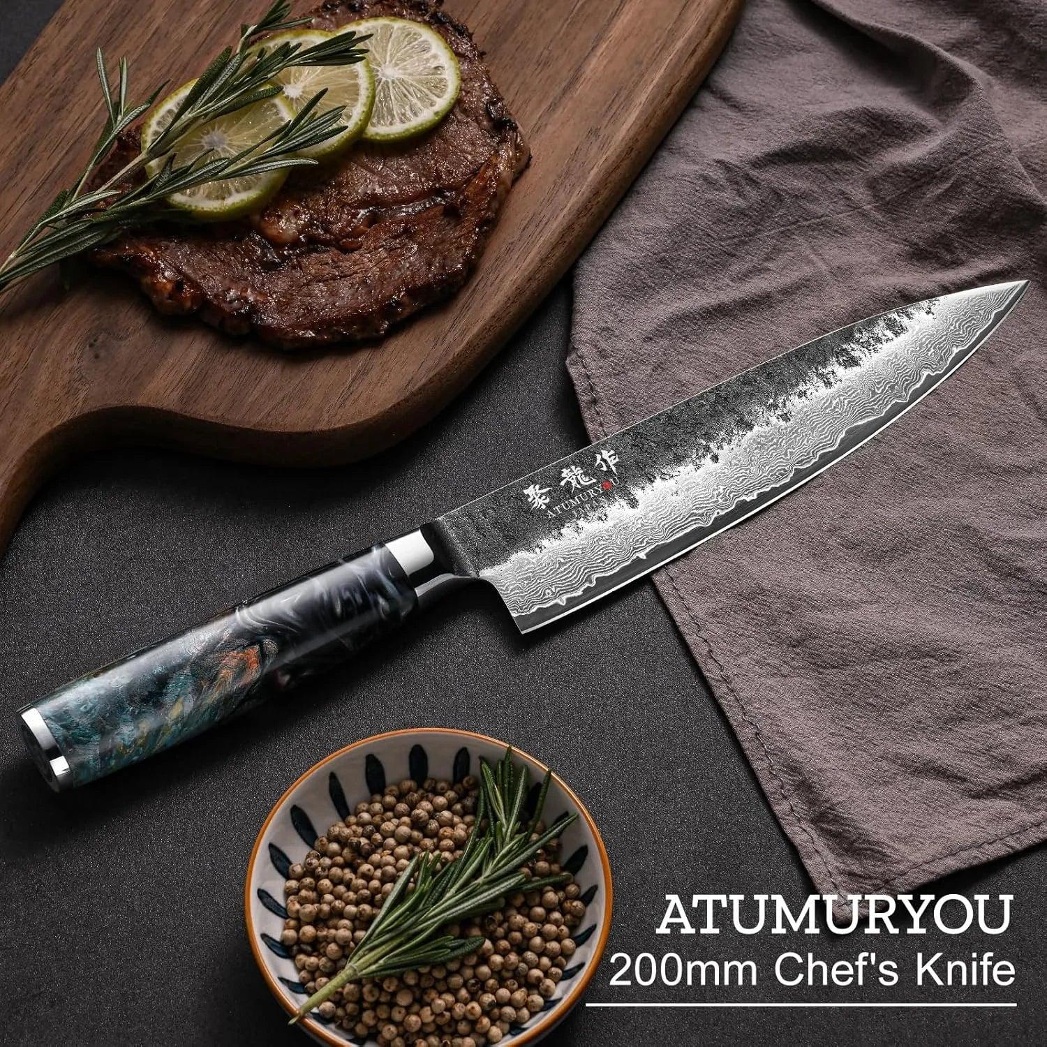 Damascus steel chef's knife with patterned blade beside steak, pepper, and rosemary on dark kitchen surface.