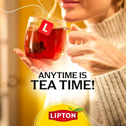 Woman sipping steaming tea from clear glass mug with Lipton tea bag, cozy sweater, warm lighting