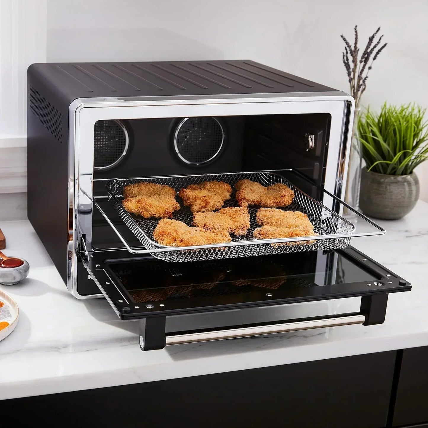 Black countertop air fryer oven with crispy chicken nuggets on mesh tray, modern kitchen appliance for healthy cooking