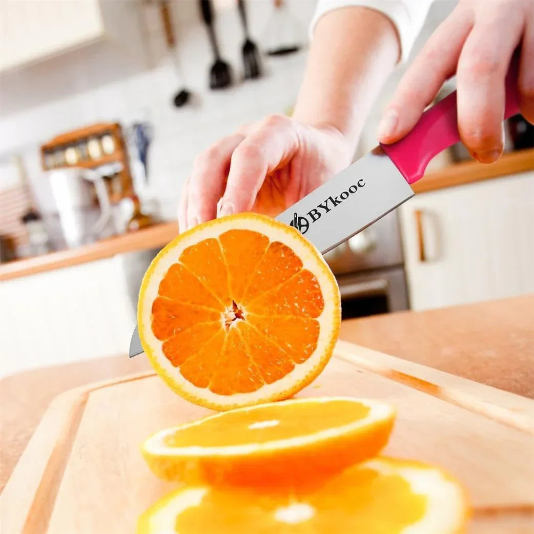 Pink-handled BYkooc kitchen knife slicing fresh orange on wooden cutting board