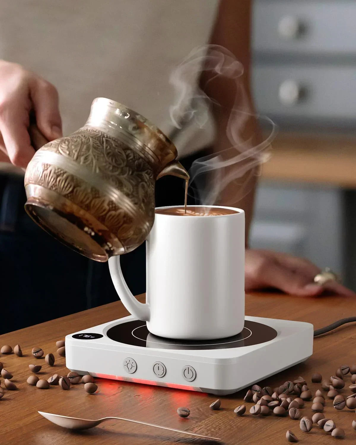 Pouring coffee from ornate kettle into white mug on electric warmer with scattered beans