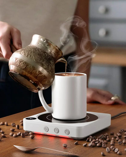 Pouring coffee from ornate kettle into white mug on electric warmer with scattered beans