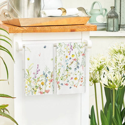 Floral kitchen towels hanging on white cart, with wooden tray and greenery in cozy kitchen setting