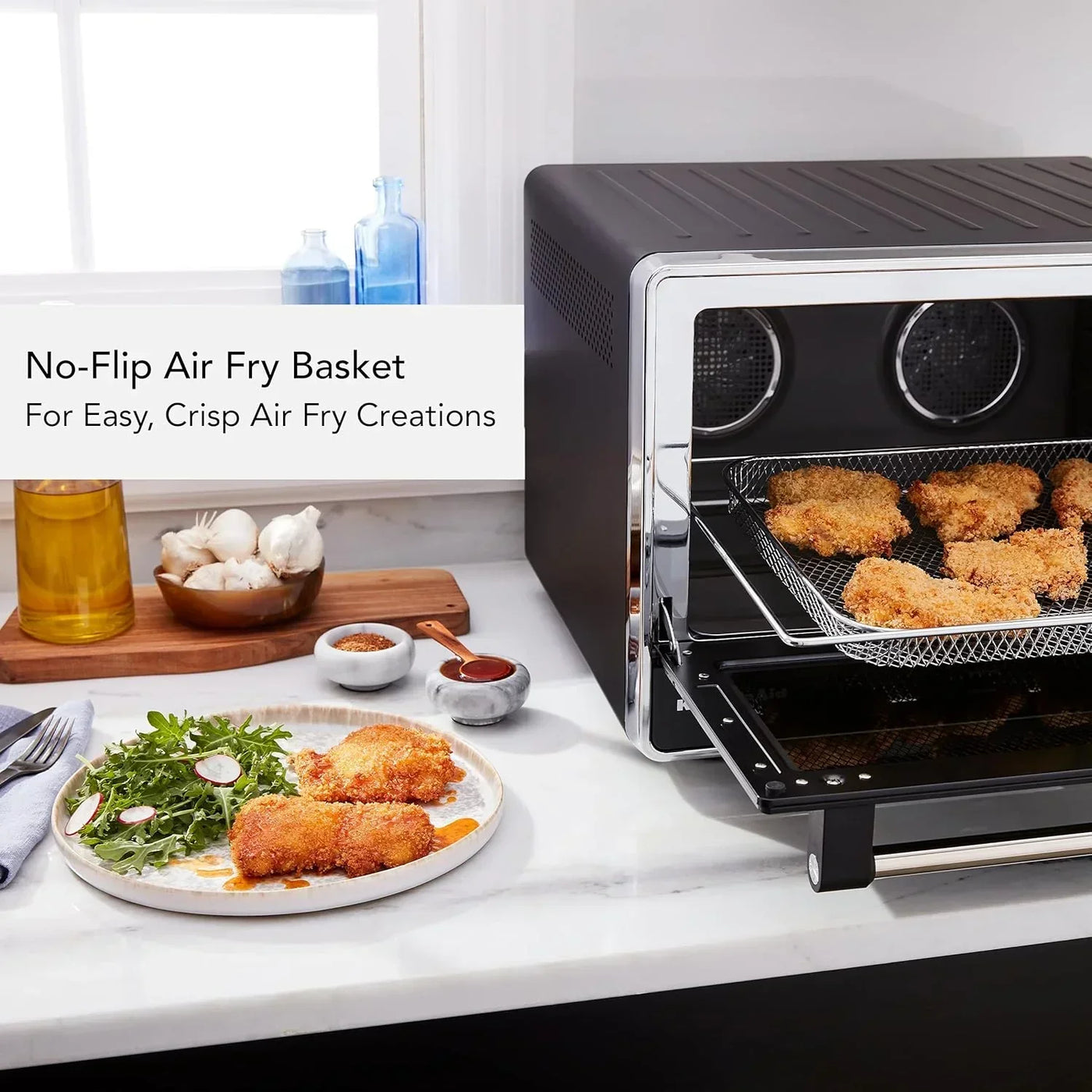 Black air fryer with no-flip basket cooking crispy chicken, served on plate with salad in modern kitchen