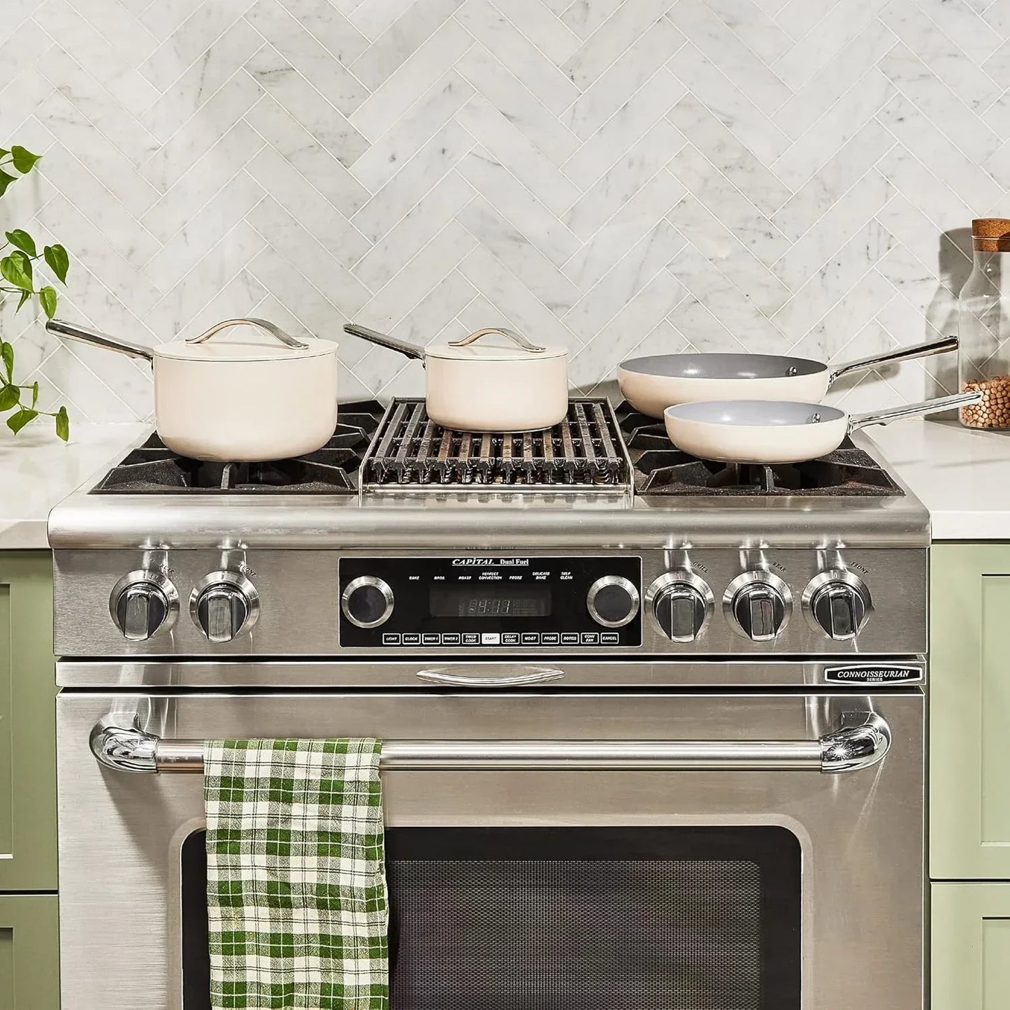 Modern kitchen stove with white cookware set, frying pans, and saucepans on countertop
