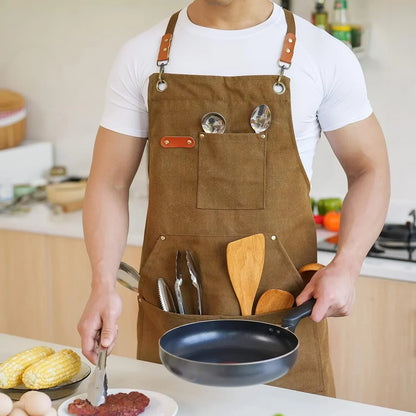 Brown canvas apron with pockets holding kitchen tools, worn while cooking in a modern kitchen