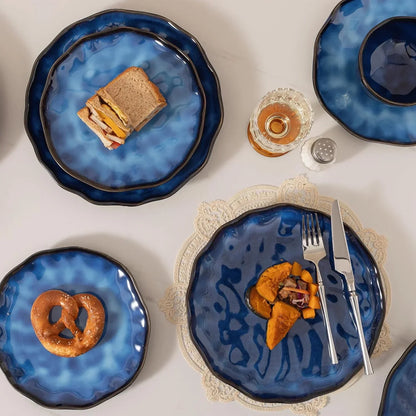 Blue ceramic dinnerware set with wavy edges, serving sandwiches, pretzel, and roasted veggies on white table