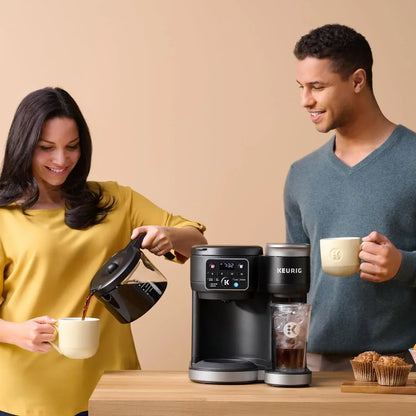 Keurig coffee maker brewing fresh coffee for morning breakfast with mugs and muffins on kitchen counter