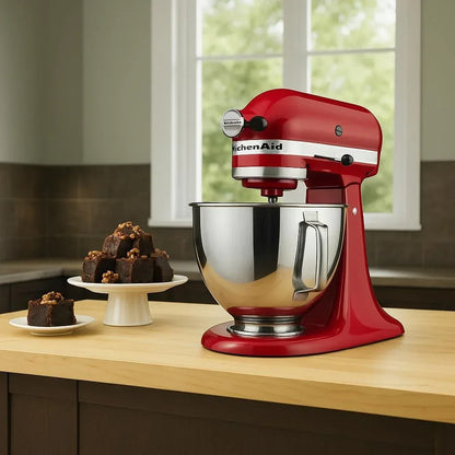 Red KitchenAid stand mixer with stainless steel bowl beside chocolate brownies on a kitchen counter