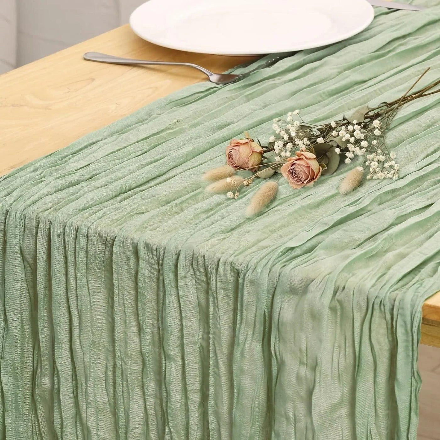 Mint green pleated table runner with dried roses and baby's breath, styled on wooden table with white plate and fork