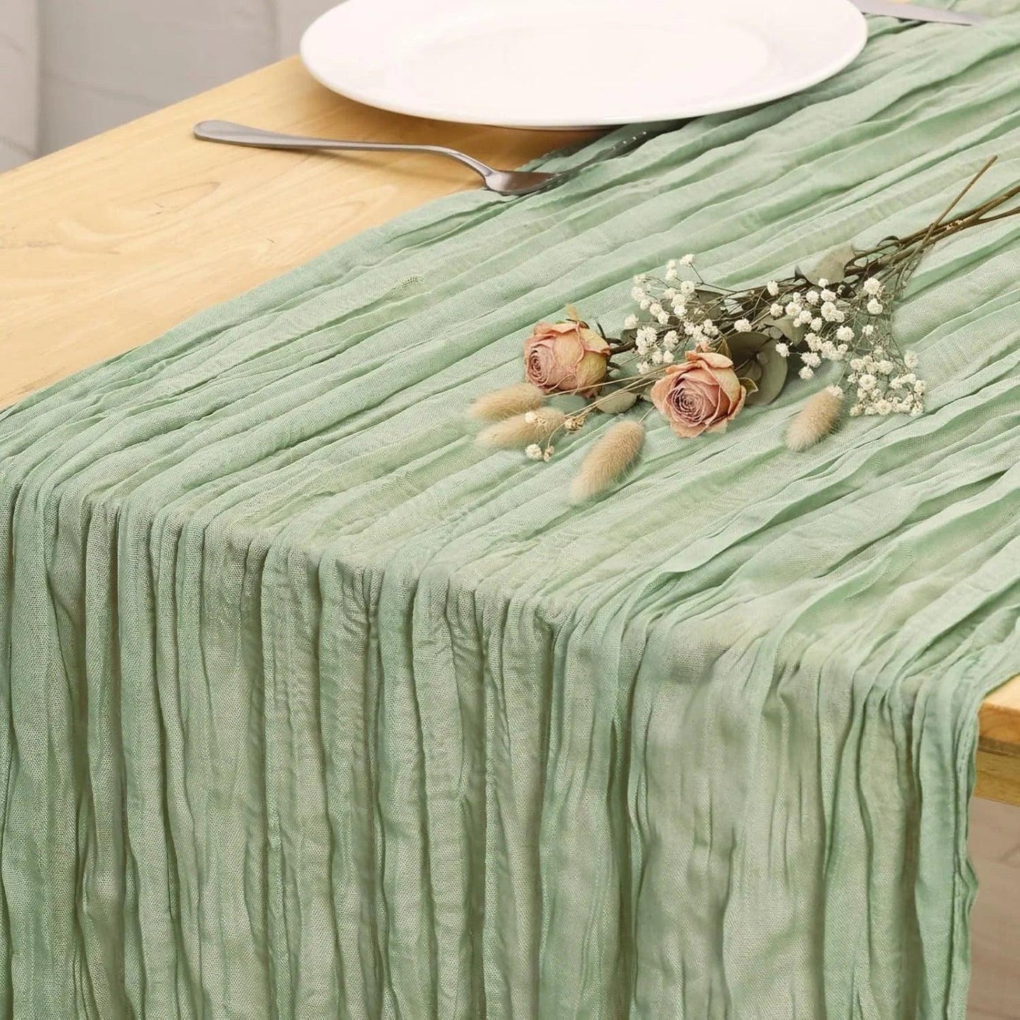 Mint green pleated table runner with dried roses and baby's breath, styled on wooden table with white plate and fork
