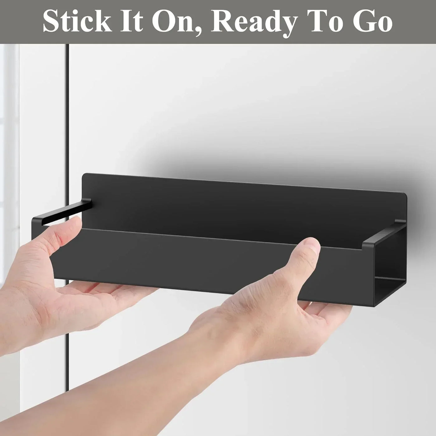Hands installing a black wall-mounted kitchen storage shelf on a light-colored surface.