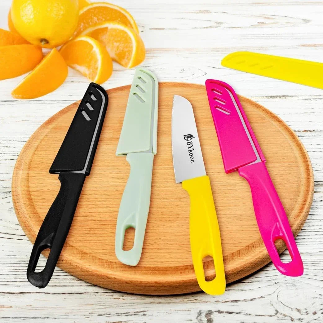 Colorful paring knives with protective sheaths on wooden cutting board, fresh oranges nearby for kitchen prep