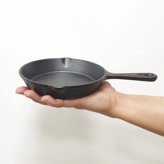 Hand holding small black cast iron skillet, ideal for everyday cooking and kitchen routines.