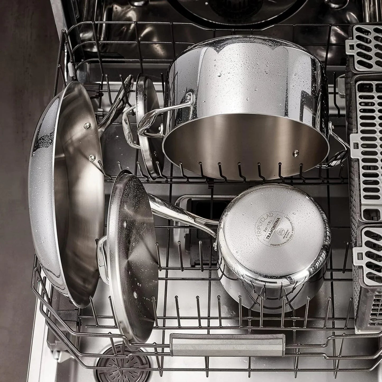 Stainless steel cookware set in dishwasher, featuring pots, pans, and lids with water droplets, ideal for kitchen cleaning and storage.