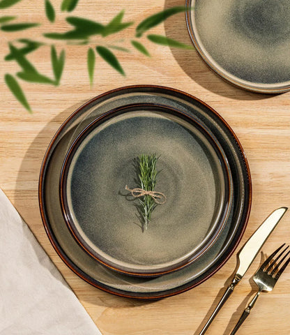 Ceramic dinner plates with rustic brown rim, rosemary sprig, and gold cutlery on wooden table