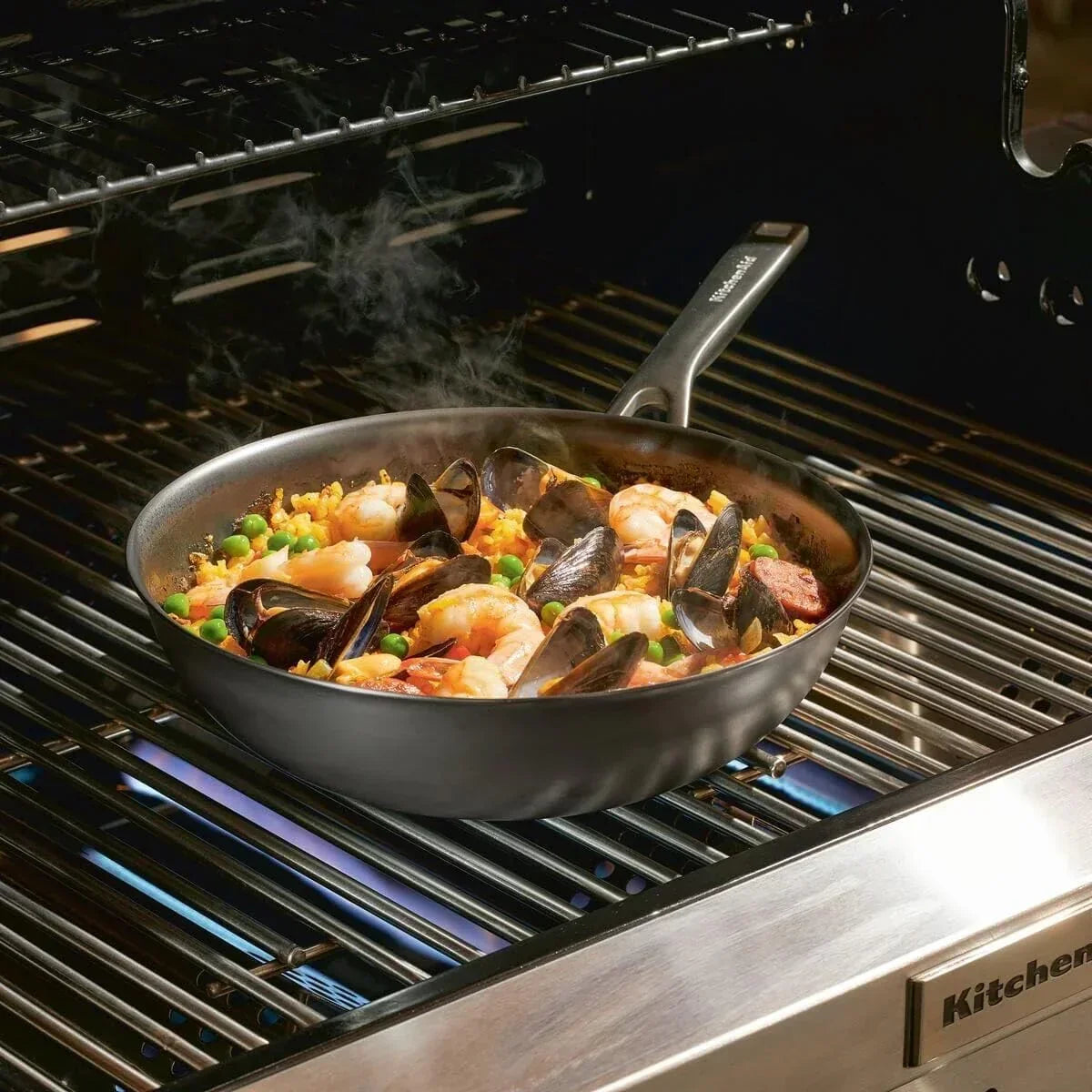 Sizzling seafood paella in a nonstick skillet on a gas grill, featuring shrimp, mussels, and peas.